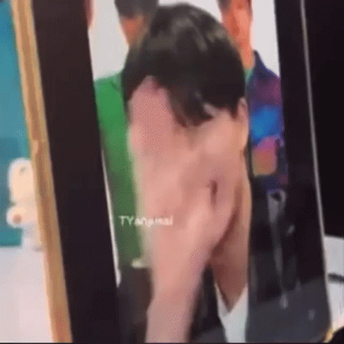 A Man Is Covering His Face With His Hand While Looking At A Picture Of Himself . GIF