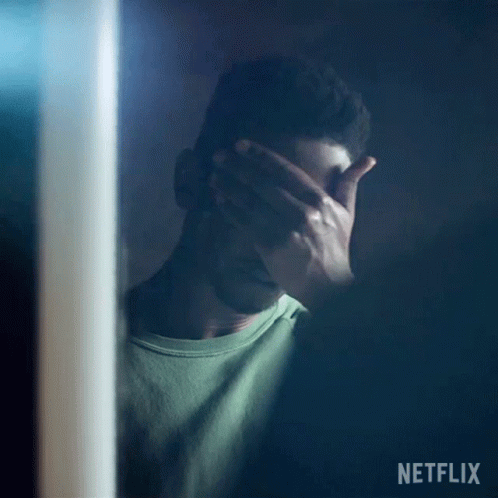 A Man Is Covering His Face With His Hand While Standing In Front Of A Mirror . GIF