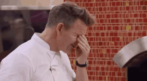 A Man Is Covering His Face With His Hands In Front Of A Red Tiled Wall . GIF