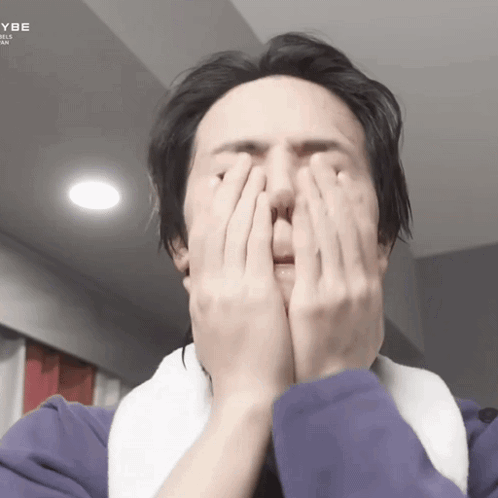 A Man Is Covering His Face With His Hands While Wearing A Purple Jacket GIF