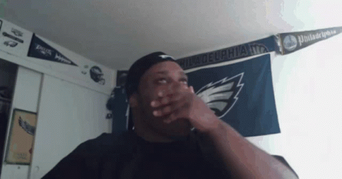 A Man Is Covering His Mouth In Front Of A Philadelphia Flag GIF