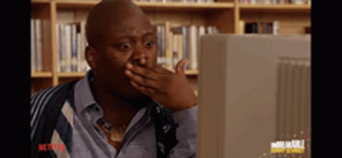 A Man Is Covering His Mouth With His Hand While Looking At A Computer Monitor . GIF