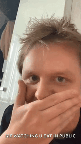 A Man Is Covering His Mouth With His Hands While Looking At The Camera . GIF