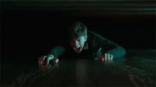 A Man Is Crawling Out Of A Hole In The Floor In The Dark . GIF