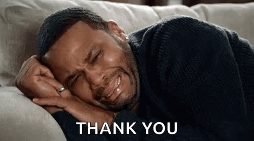 A Man Is Crying While Laying On A Couch With The Words `` Thank You '' Behind Him . GIF