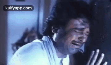 A Man Is Crying While Leaning Against A Wall With His Eyes Closed . GIF