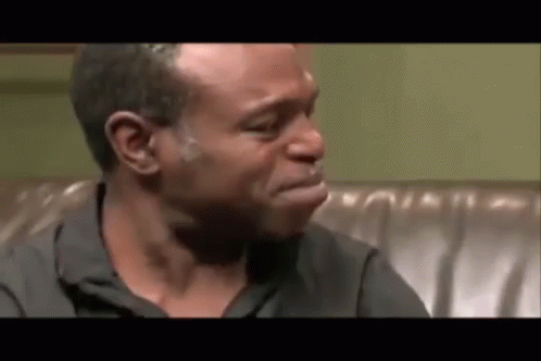 A Man Is Crying While Sitting On A Couch With His Mouth Open . GIF