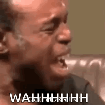 A Man Is Crying While Sitting On A Couch With His Mouth Open And The Words Wahh Written On His Face . GIF