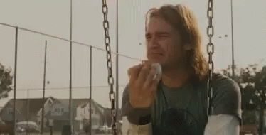 A Man Is Crying While Sitting On A Swing And Eating A Sandwich . GIF