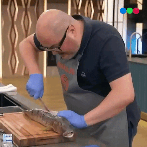 A Man Is Cutting A Fish On A Cutting Board While Wearing A Shirt That Says Benetton GIF