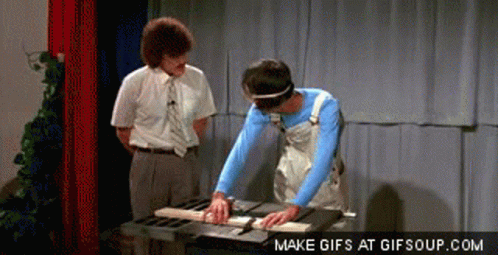 a man is cutting a piece of wood on a table saw while another man looks on