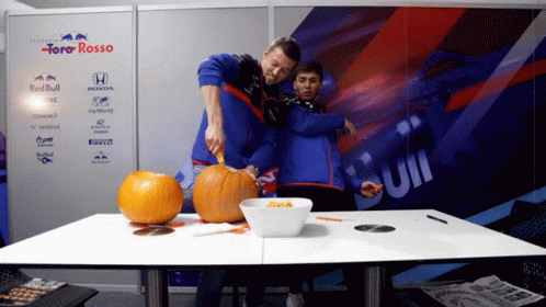 A Man Is Cutting A Pumpkin In Front Of A Wall That Says Toro Rosso GIF