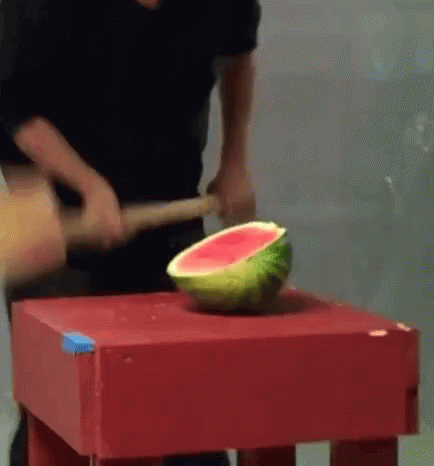 A Man Is Cutting A Watermelon With A Hammer On A Table . GIF