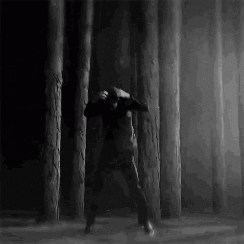 A Man Is Dancing In A Dark Forest Surrounded By Trees . GIF