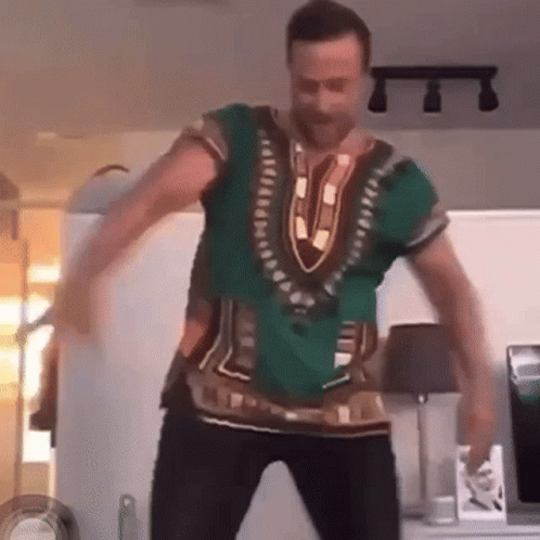 A Man Is Dancing In A Living Room Wearing A Green Shirt . GIF
