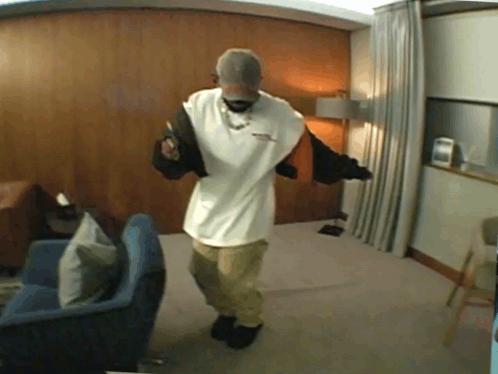 A Man Is Dancing In A Living Room Wearing A Hat And A White Shirt GIF
