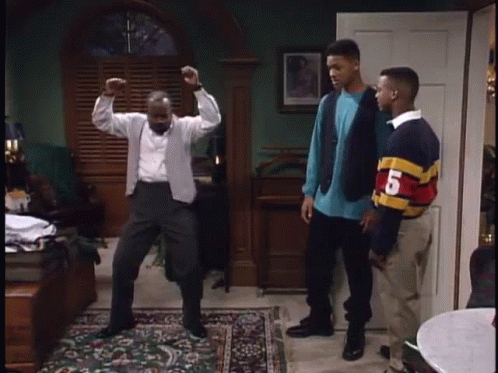 A Man Is Dancing In A Living Room While Two Other Men Stand Behind Him . GIF