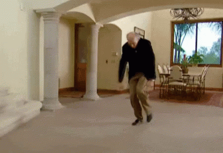A Man Is Dancing In A Living Room With Columns And A Dining Table . GIF