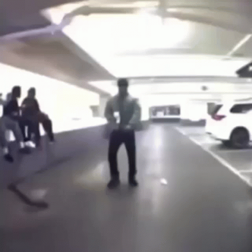 A Man Is Dancing In A Parking Garage While A Group Of People Sit On A Bench . GIF