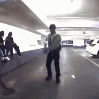 A Man Is Dancing In A Parking Garage With People Sitting On Benches . GIF