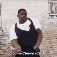 A Man Is Dancing In Front Of A Brick Wall With The Words `` You Coming Home Today ! Yay '' Written On It . GIF