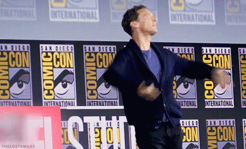 A Man Is Dancing In Front Of A Comic Con Banner GIF