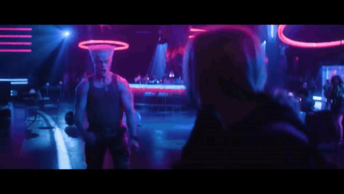 A Man Is Dancing In Front Of A Crowd In A Club With Purple And Blue Lights . GIF