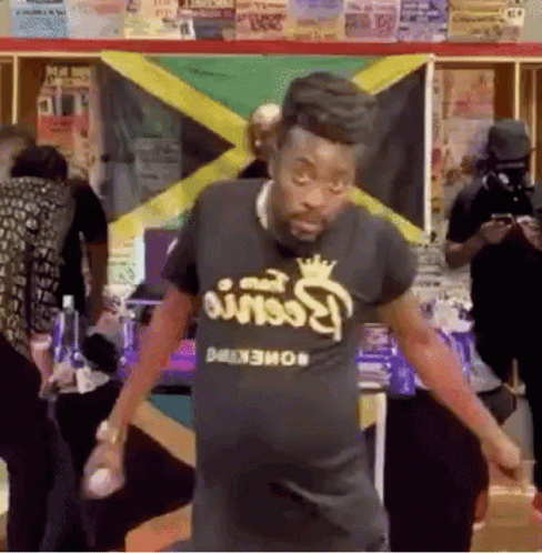 A Man Is Dancing In Front Of A Jamaican Flag In A Room . GIF