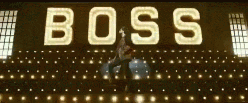 A Man Is Dancing In Front Of A Large Sign That Says Boss GIF