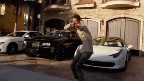 A Man Is Dancing In Front Of A Row Of Cars In A Driveway . GIF