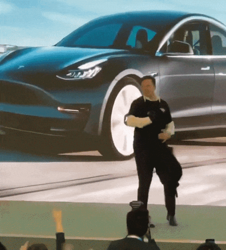 A Man Is Dancing In Front Of A Tesla Model 3 Car GIF
