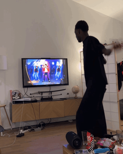 A Man Is Dancing In Front Of A Tv That Shows A Dance Video GIF