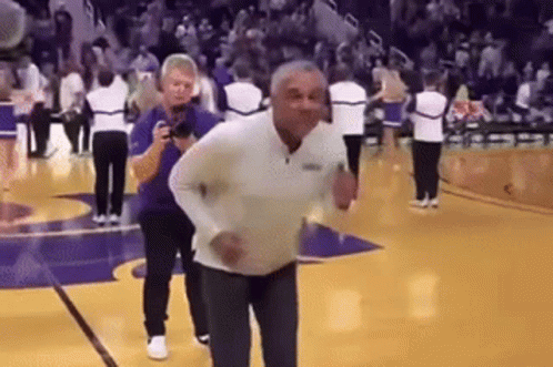 A Man Is Dancing On A Basketball Court While A Man Takes A Picture Of Him . GIF