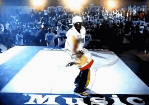 A Man Is Dancing On A Dance Floor In Front Of A Crowd With A Sign That Says Music GIF