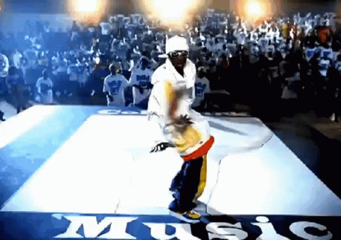 A Man Is Dancing On A Dance Floor In Front Of A Crowd With The Word Music Written On The Floor GIF