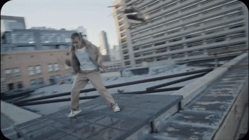 A Man Is Dancing On A Rooftop In Front Of A City Skyline GIF