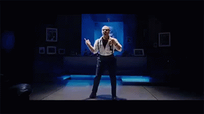 A Man Is Dancing On A Stage In A Dark Room . GIF