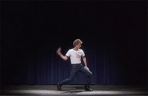 A Man Is Dancing On A Stage With A Blue Curtain Behind Him . GIF