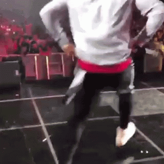 A Man Is Dancing On A Stage With A Crowd Watching . GIF
