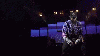 A Man Is Dancing On A Stage With A Knife In His Hand In A Dark Room . GIF