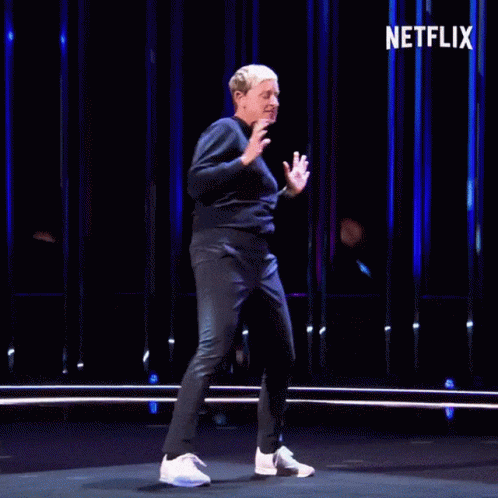 A Man Is Dancing On A Stage With The Netflix Logo In The Background GIF