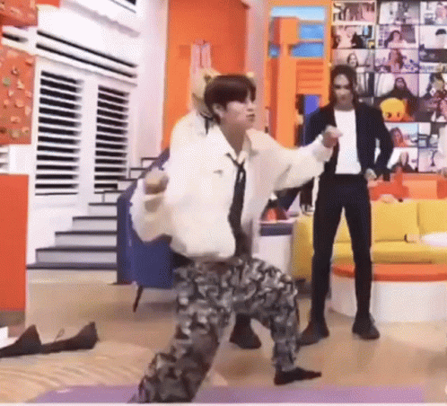 A Man Is Dancing On A Yoga Mat In A Living Room While A Man Stands Behind Him . GIF