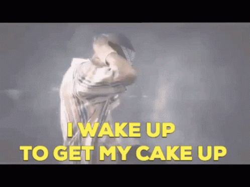 A Man Is Dancing With The Words " I Wake Up To Get My Cake Up " Behind Him GIF