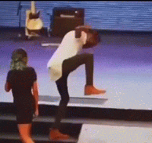 A Man Is Doing A Handstand On A Stage While A Woman Watches . GIF