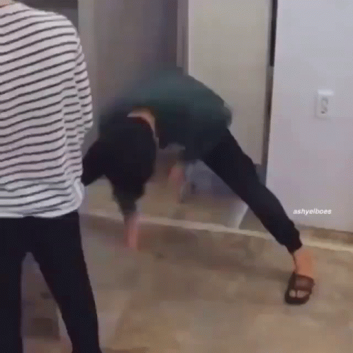 A Man Is Doing A Handstand On The Floor In Front Of A Mirror While Another Man Stands Behind Him . GIF