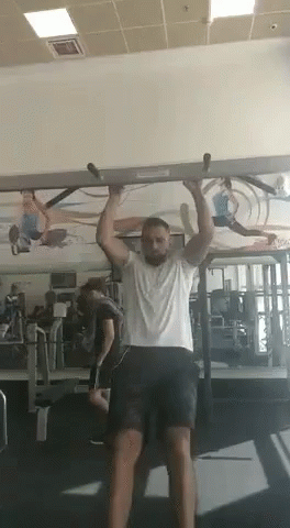 A Man Is Doing A Pull Up Exercise In A Gym . GIF