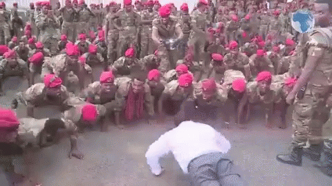 A Man Is Doing Push Ups In Front Of A Large Group Of Soldiers Wearing Red Hats . GIF