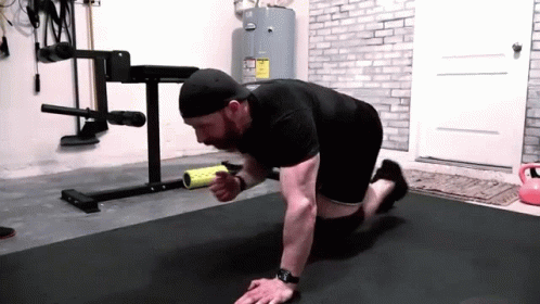 A Man Is Doing Push Ups On A Mat In A Gym While Holding A Roller . GIF