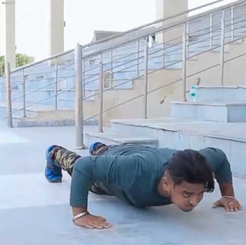 A Man Is Doing Push Ups On A Sidewalk In Front Of Some Stairs GIF