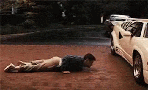 A Man Is Doing Push Ups On The Ground In Front Of A White Car GIF